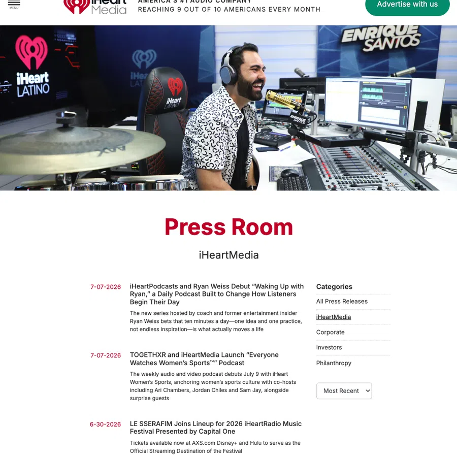 Radio host Enrique Santos speaking into microphone in iHeart Latino studio with audio equipment and drum set visible