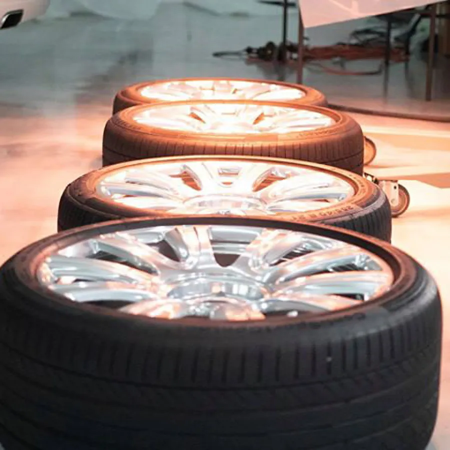 Four car tires with shiny silver rims lined up on a workshop floor with warm lighting.