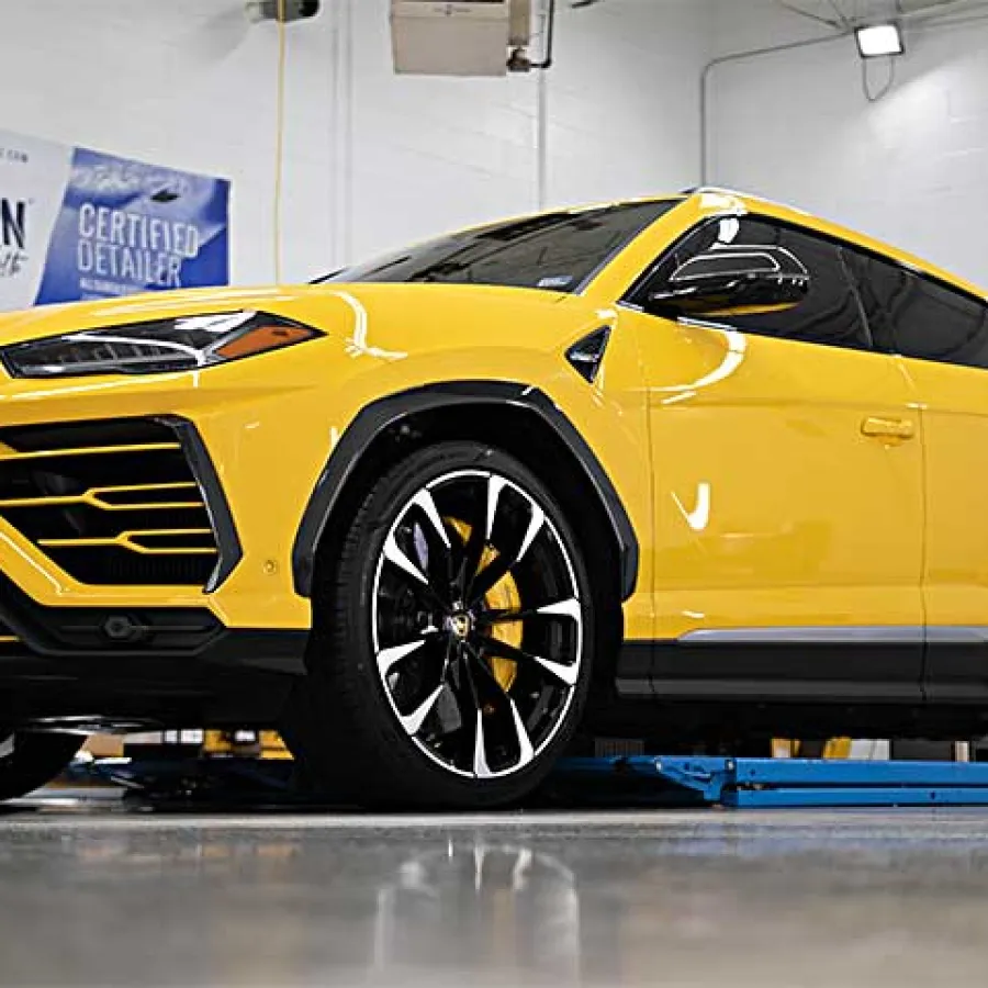 Yellow luxury Lamborghini SUV parked inside a modern detailing garage with black accents and large wheels.