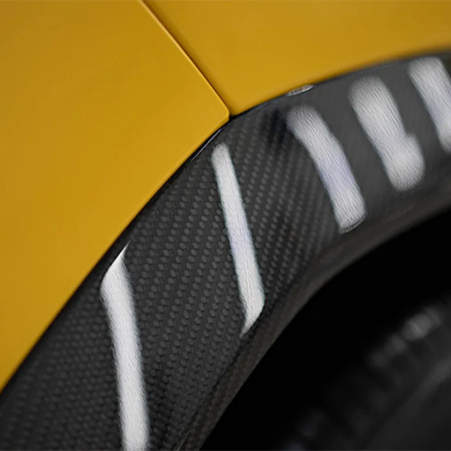 Close-up of a yellow car fender with a carbon fiber trim and tire visible in the background.