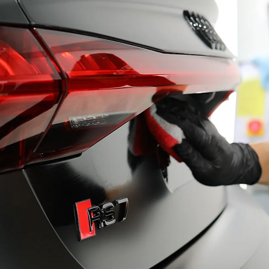 Close-up of a person cleaning the rear of a black Audi RS7 near the taillight during detailing.