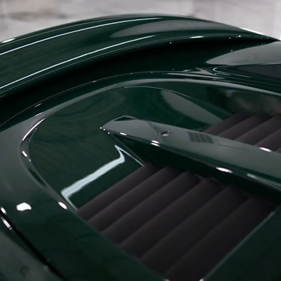 Close-up of dark green vintage car hood with sleek ventilation slats and shiny curved surface.