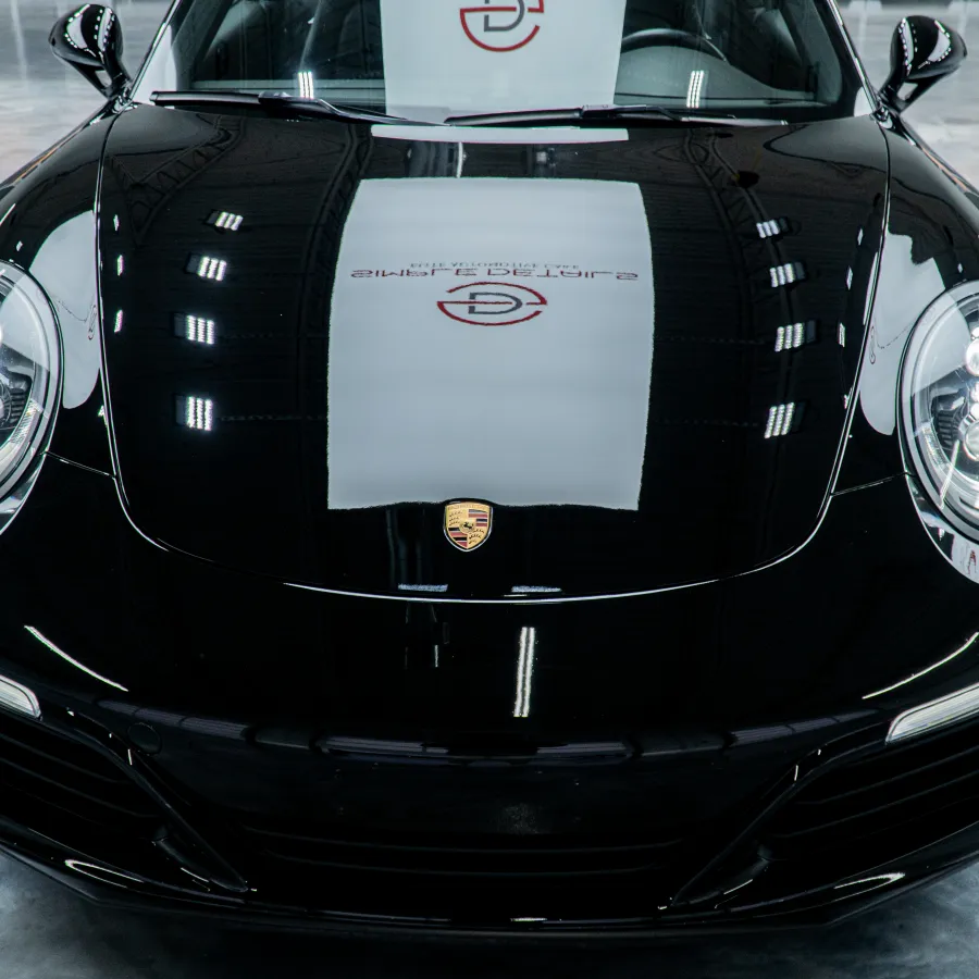 Front view of a shiny black Porsche sports car with headlights on in a reflective showroom.