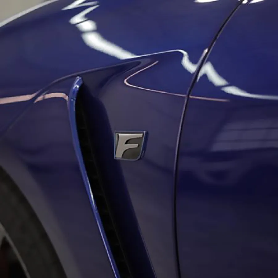 Close-up of a blue car fender with an F badge and air vent near the front wheel.