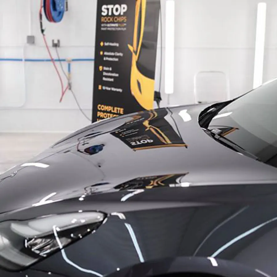 Close-up of a shiny black car hood reflecting a workshop interior and promotional banner.