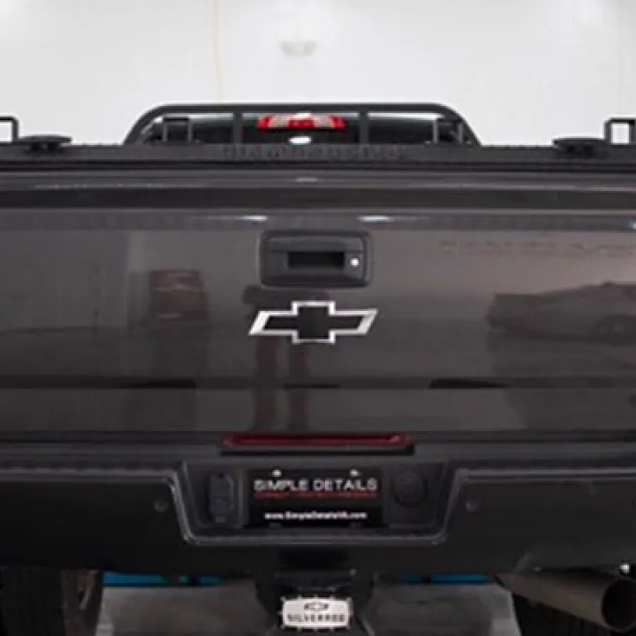 Rear view of gray Chevrolet Silverado truck inside a garage with visible logo and license plate.