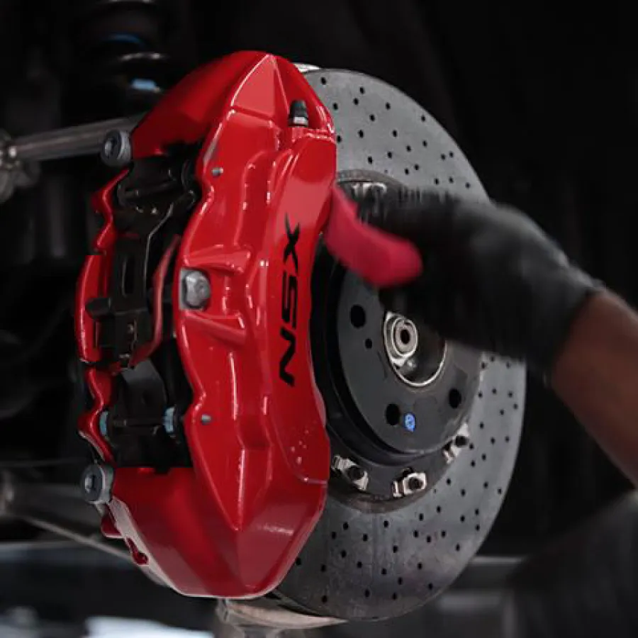 Close-up of a red NSX brake caliper and perforated brake disc with a gloved hand cleaning the caliper.