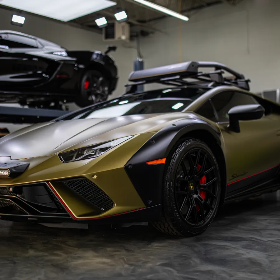 Gold and black Lamborghini sports car with roof rack inside a garage with another black car in background.