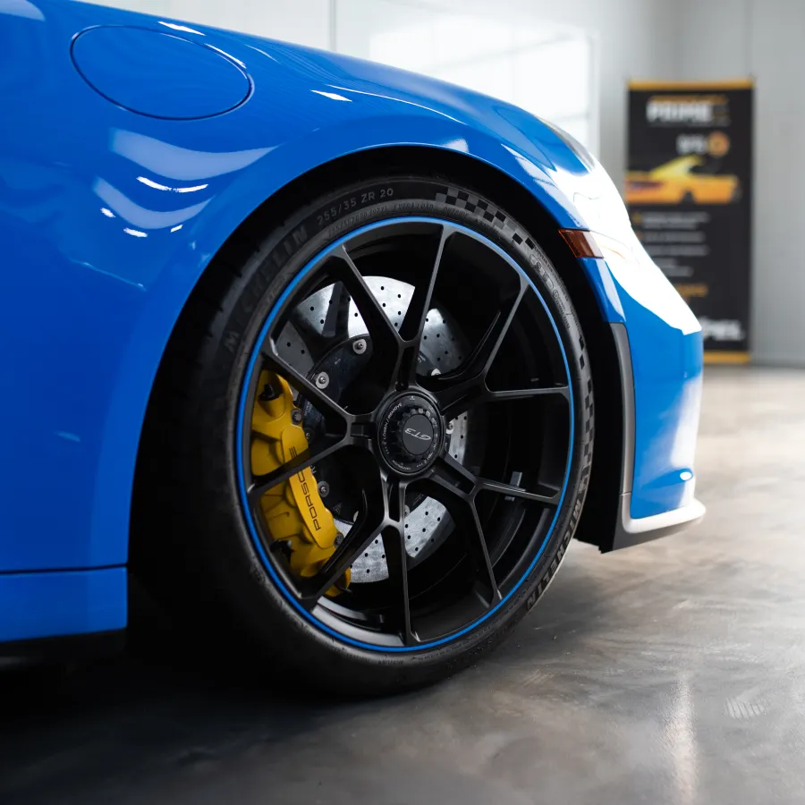 Close-up of a blue sports car wheel with black alloy rim and yellow brake caliper in a showroom.