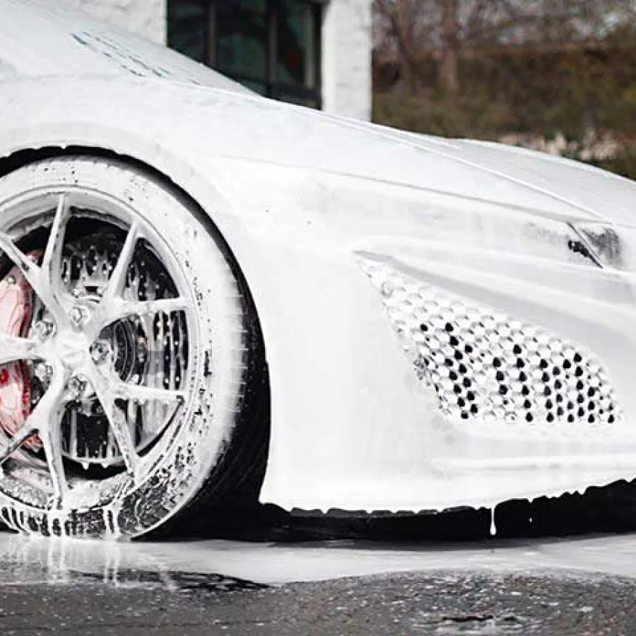 White sports car covered in thick foam during a wash with focus on the front wheel and fender