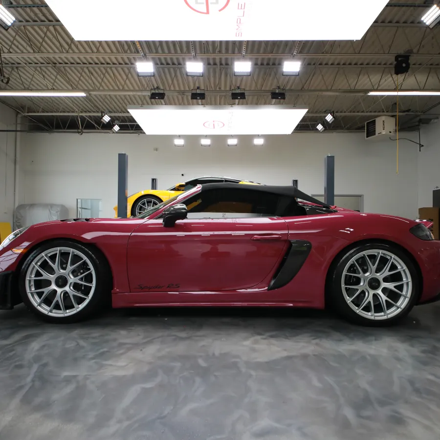 Red sports convertible car parked inside a spacious, well-lit garage with a yellow car visible in the background.