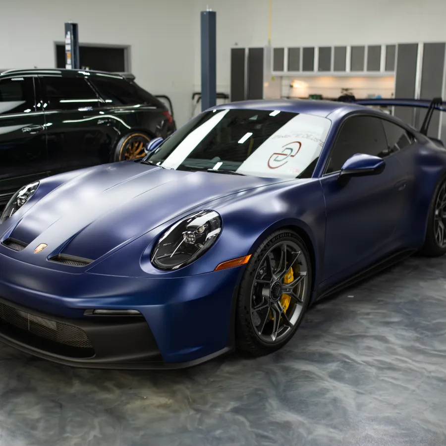 Matte blue Porsche sports car with black rims and yellow brake calipers in a polished garage setting.
