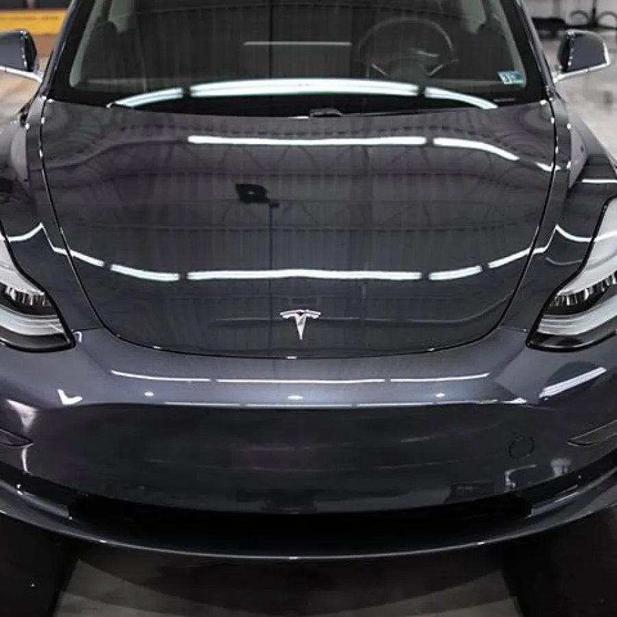 Front view of a sleek dark gray Tesla electric car parked indoors on a smooth concrete floor