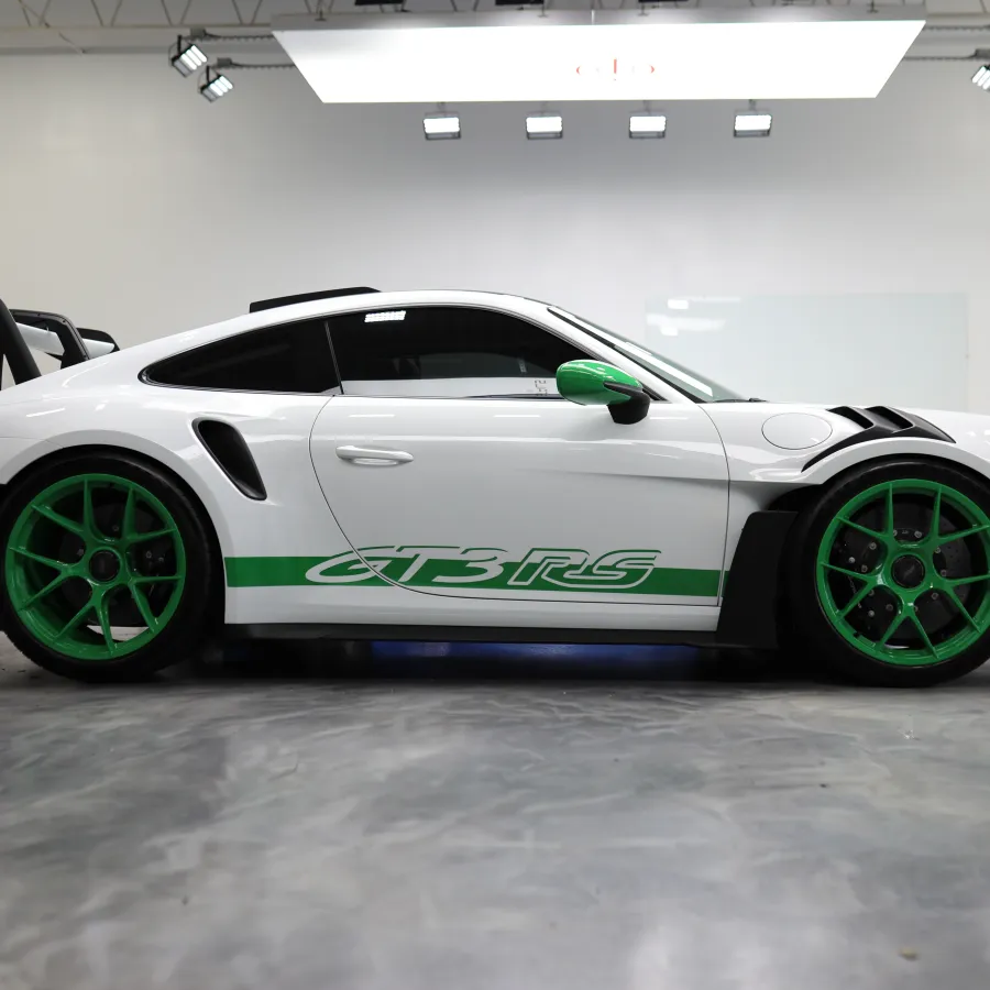White Porsche GT3 RS with green wheels and accents parked in a bright indoor garage.
