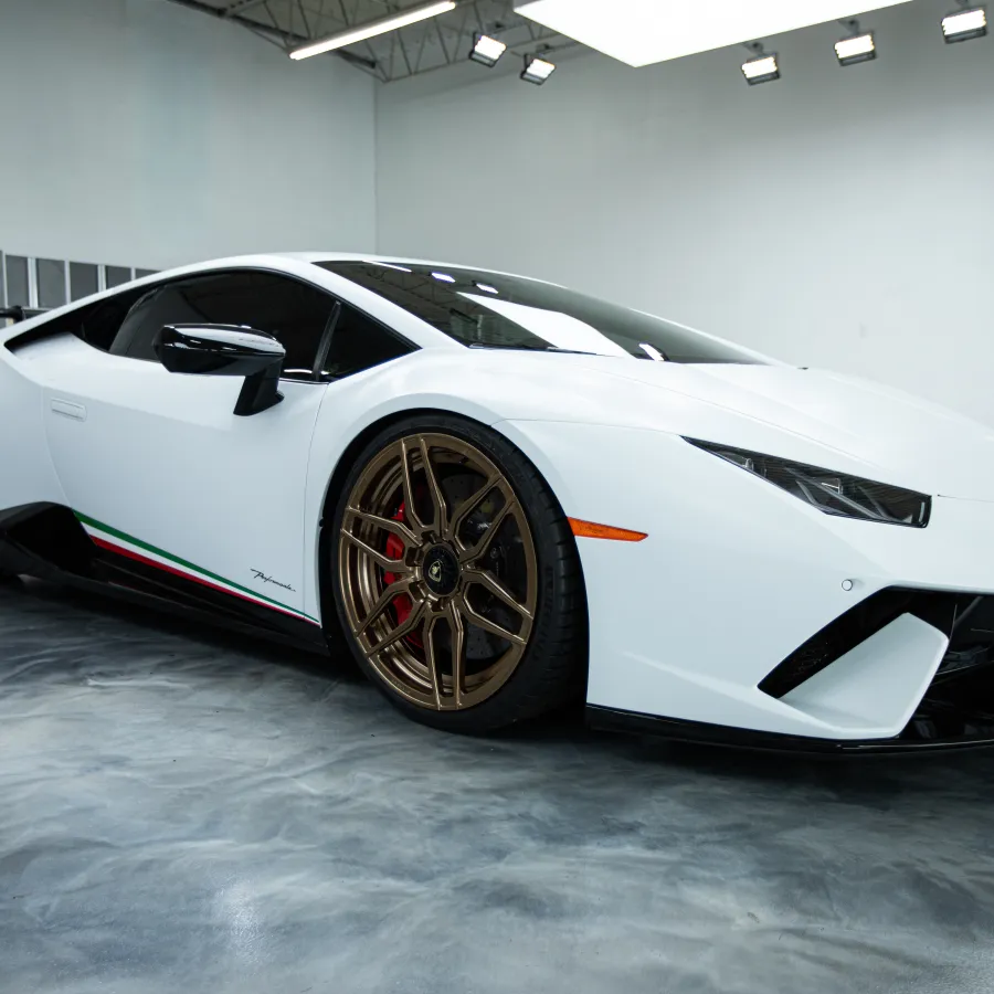 White Lamborghini Huracán with bronze wheels in a bright indoor showroom with polished concrete floor.