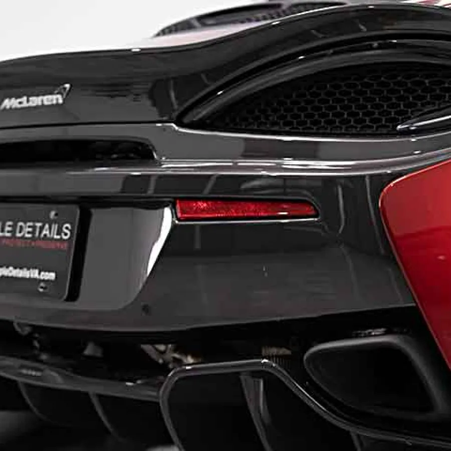 Rear close-up of a black and red McLaren sports car highlighting exhaust and tail light details.