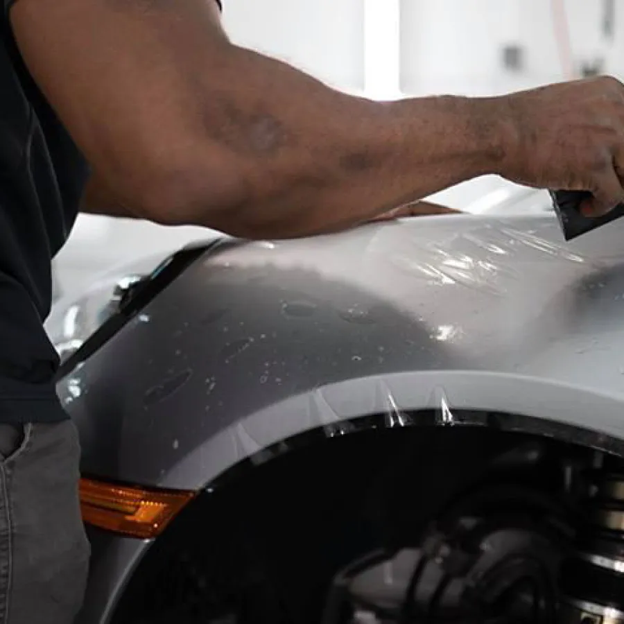 Man applying protective film on silver car fender in detailing workshop with smoothing tool