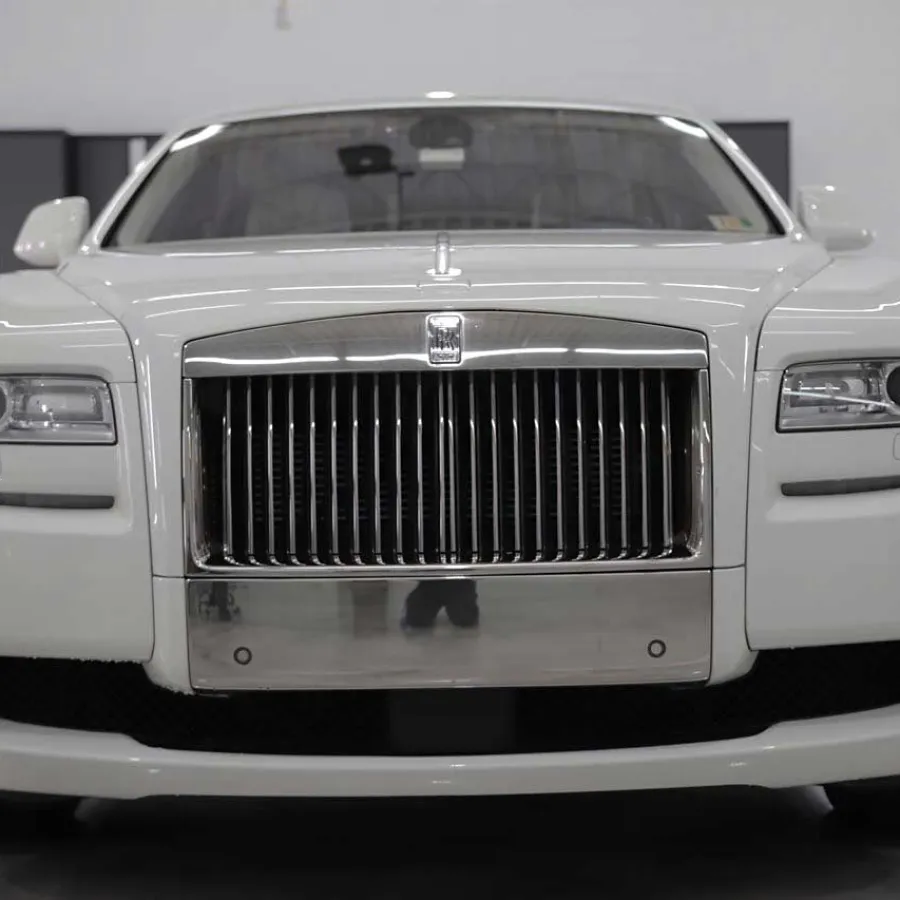 Front view of a white luxury Rolls-Royce car showcasing its iconic grille and headlights in a showroom.