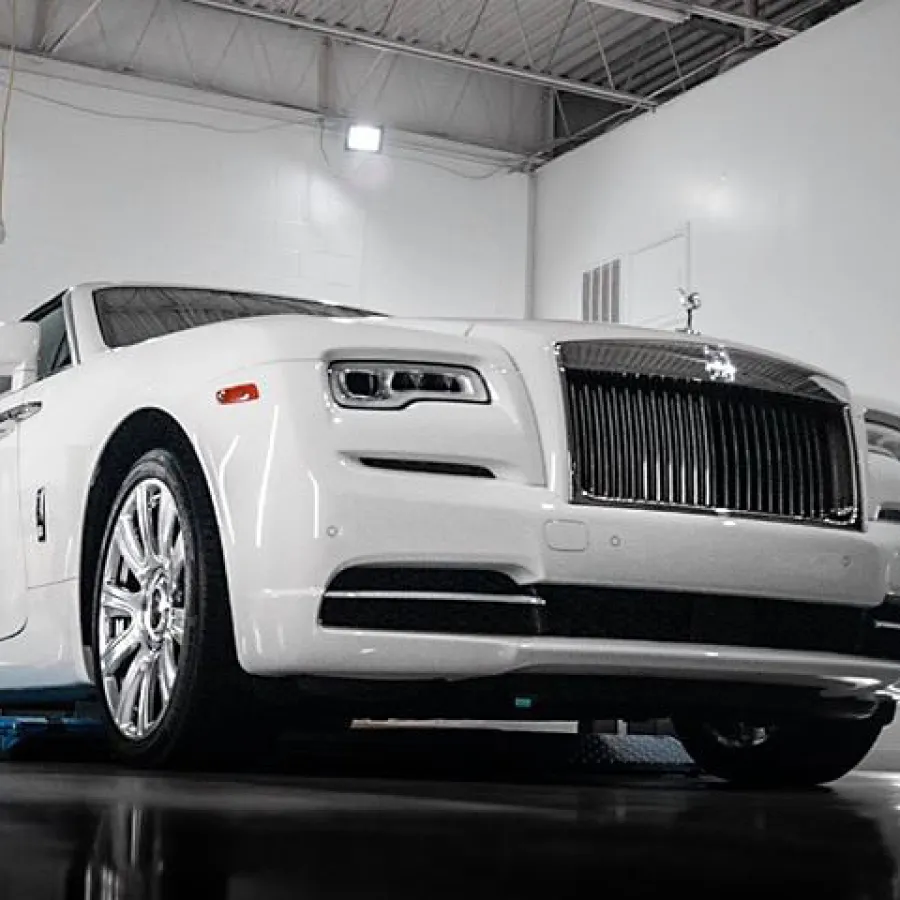 White luxury Rolls-Royce car parked inside a modern, well-lit garage with sleek interior and polished floor.