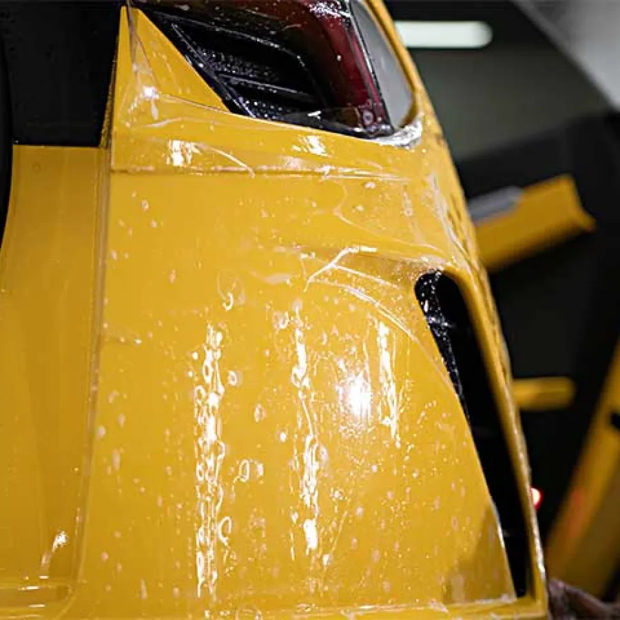 Close-up of a yellow car door with water droplets and a sleek black handle in a garage setting