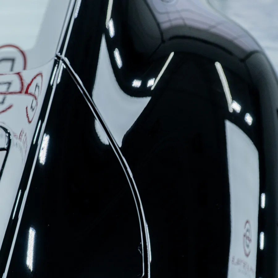 Close-up of a shiny black classic car's rear fender and vented engine cover with reflections of the indoor showroom.