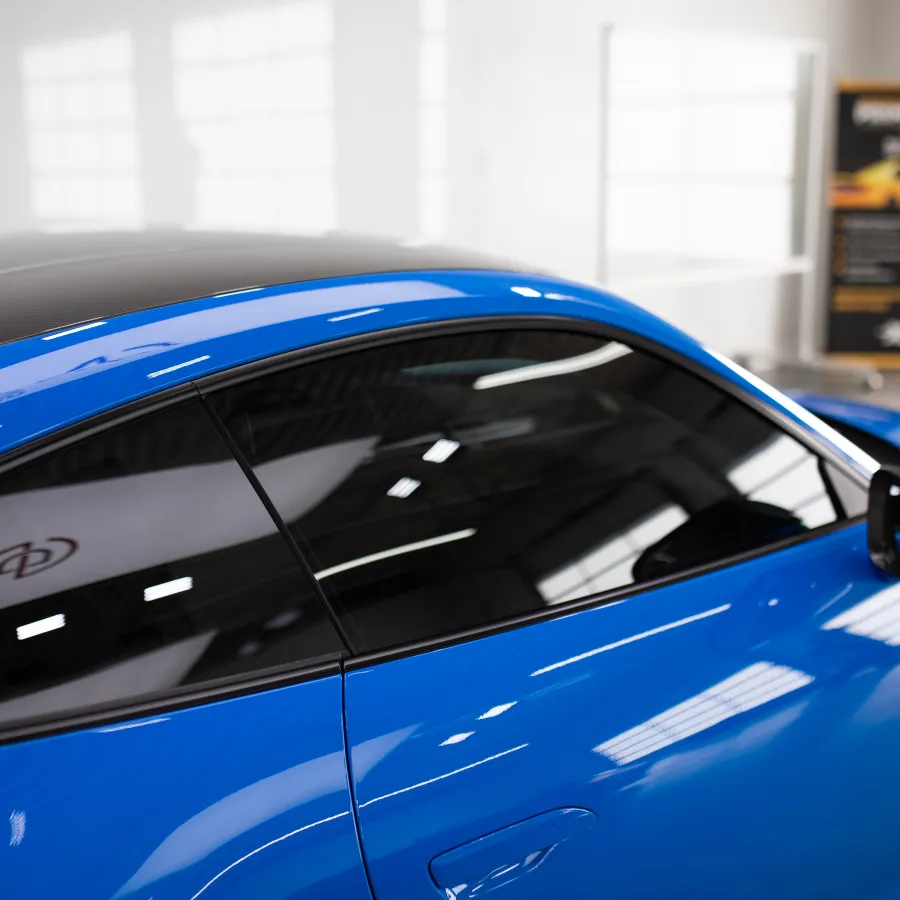Close-up of sleek blue sports car side with glossy finish and tinted windows in bright showroom.