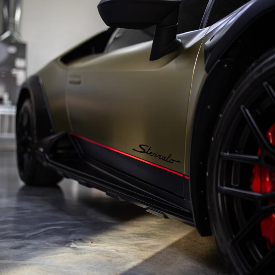 Close-up of a matte gold luxury sports car side with red accents and black wheel with red brake calipers.