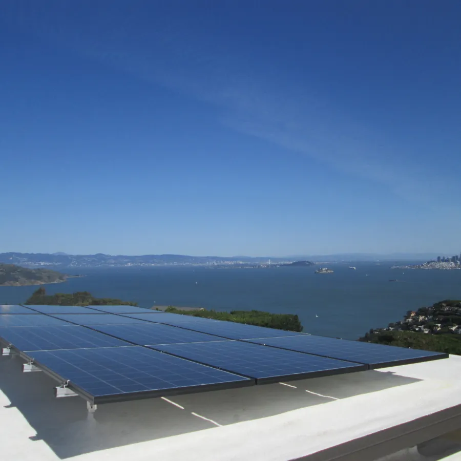 Solar panels installed on a sausalito rooftop overlooking a bay with a city skyline in the background under a clear blue sky.