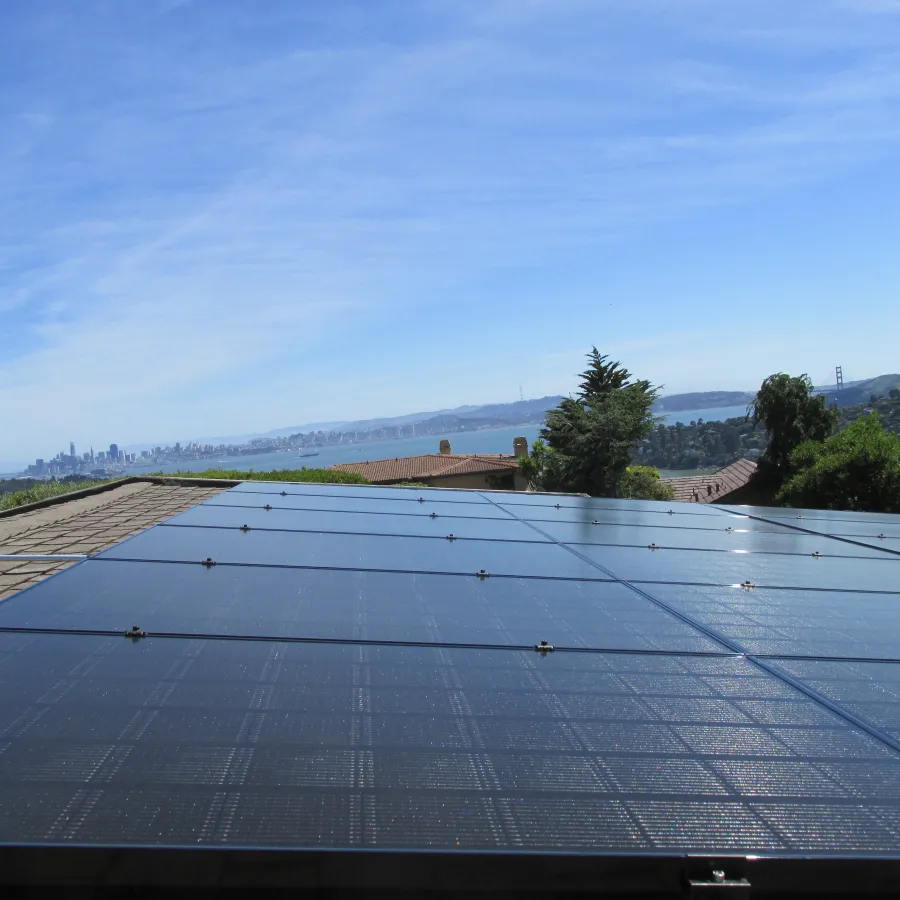 Solar panels installed on a sausalito rooftop with San Francisco skyline and Golden Gate Bridge in the background under blue sky.