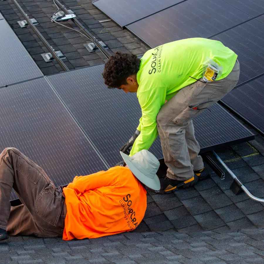 Two workers installing solar panels on a roof with safety gear and bright work shirts in daylight.