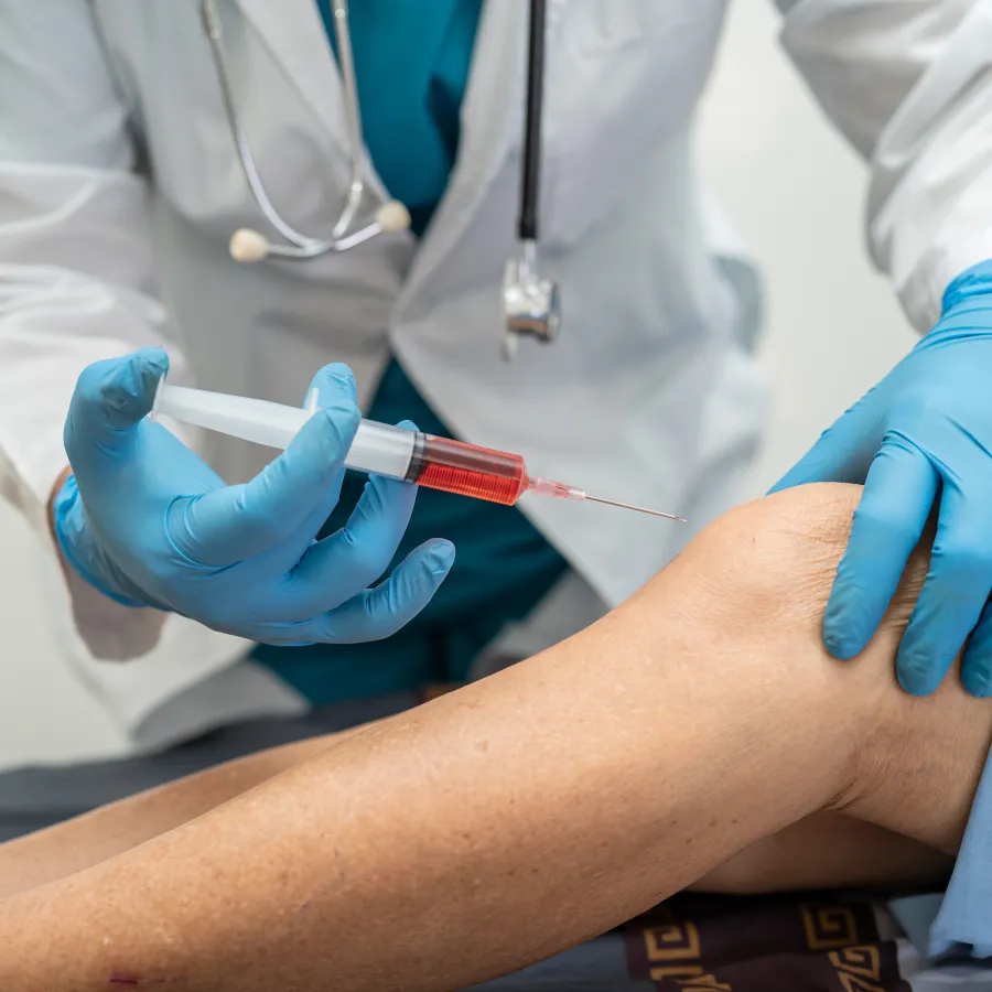Doctor wearing gloves injecting a syringe into a patient's bent knee for treatment or pain relief.