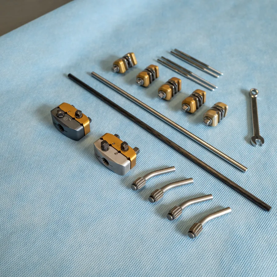 Set of mechanical tools and parts including wrenches, metal rods, clamps, and connectors arranged on blue fabric.
