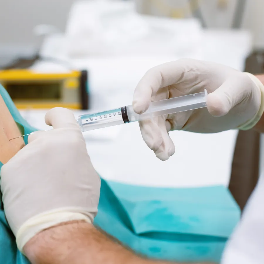 Doctor wearing gloves injecting medication with syringe into patient’s shoulder during treatment.