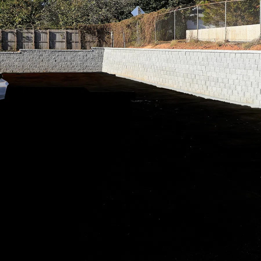 White car parked beside a newly built concrete retaining wall under bright sunlight near a wooden fence.