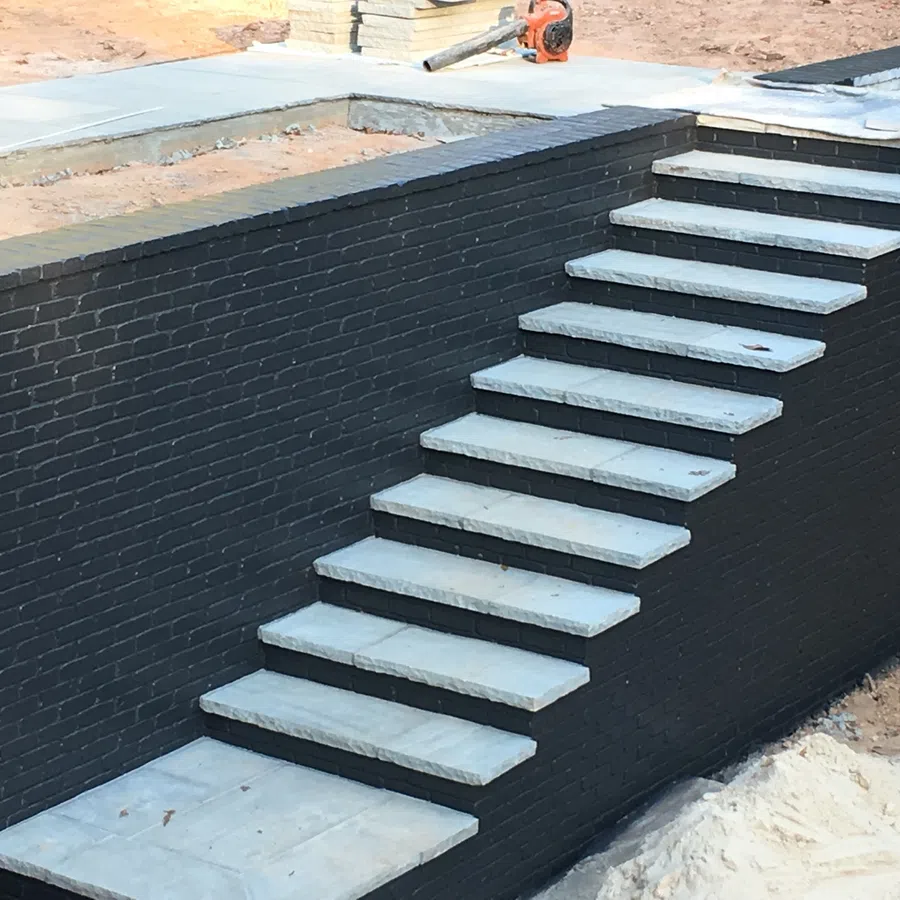 Modern outdoor stone staircase with black brick wall under construction.