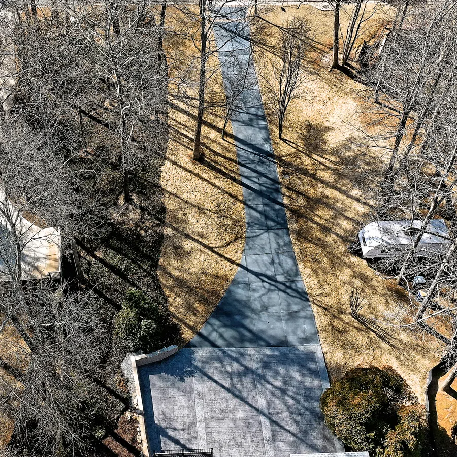 Aerial view of a curved driveway with long tree shadows on dry grass and leafless trees around homes.