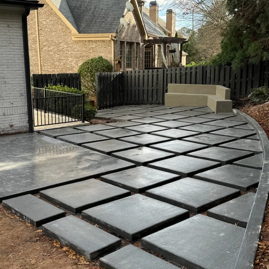 Modern backyard patio with geometric concrete pavers and built-in corner seating surrounded by a black fence.