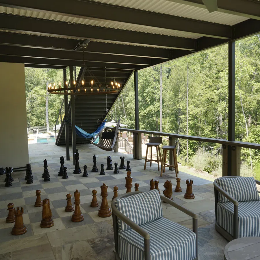 Covered outdoor patio with giant chess set, striped armchairs, hammock, bar stools, and forest view