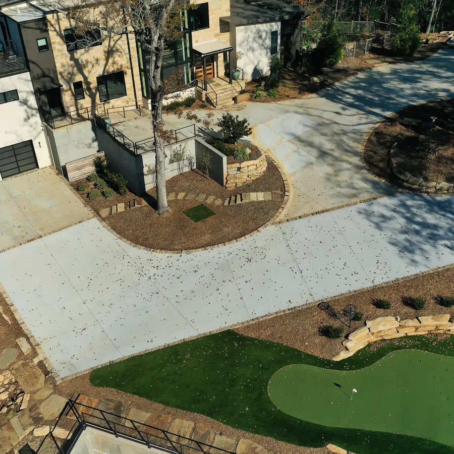 Aerial view of modern house with large driveway, landscaped garden, and a small golf putting green.