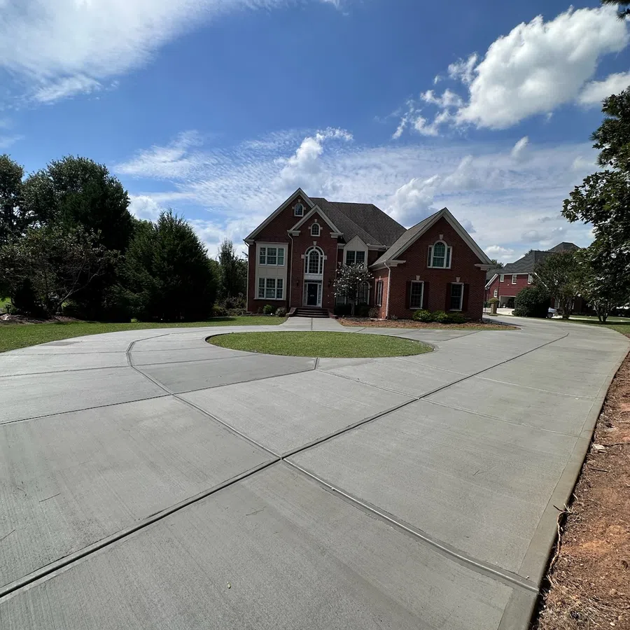 Large brick house with a circular concrete driveway under a partly cloudy blue sky.