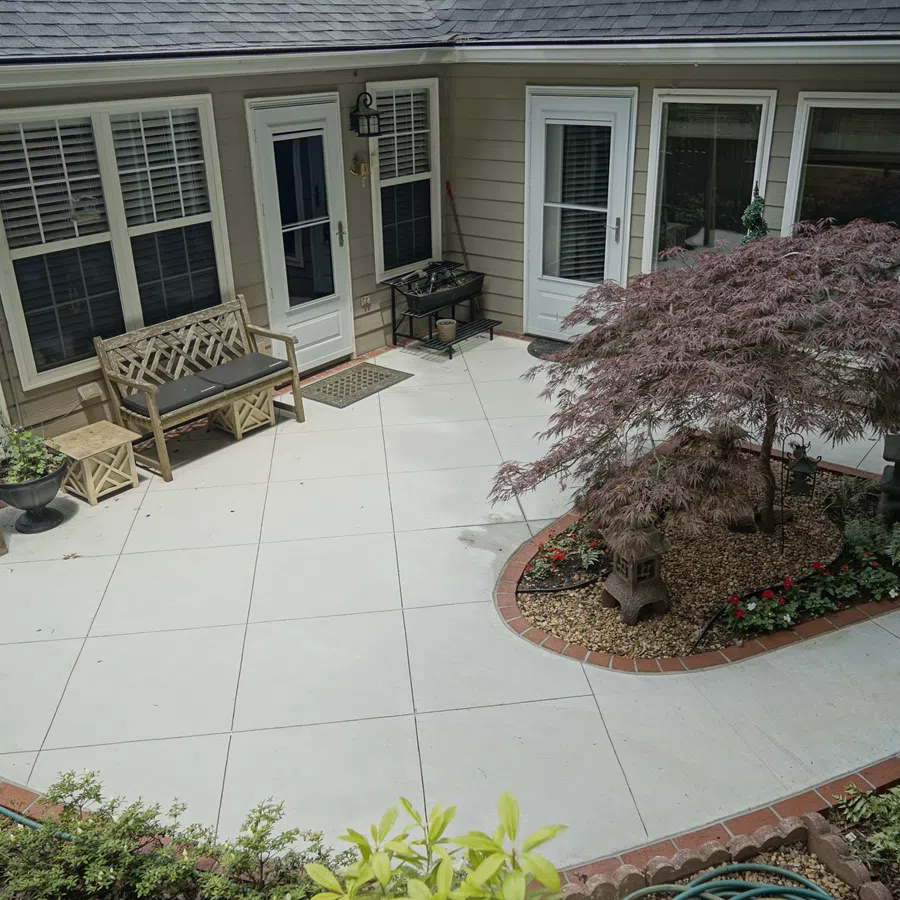 Spacious backyard patio with concrete flooring, wooden bench, small table, and landscaped garden area.