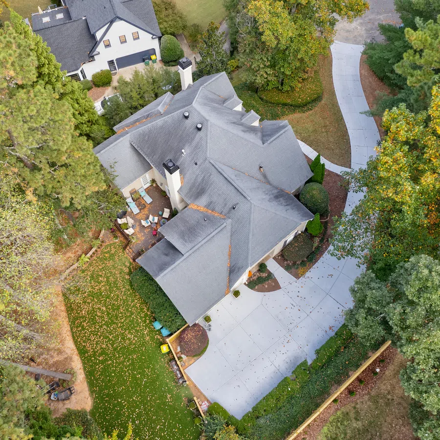 Aerial view of a suburban house with a gray roof, concrete driveway, patio, and surrounding trees in autumn.