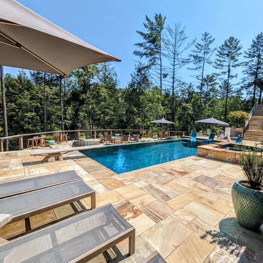 Outdoor swimming pool with sun loungers, umbrellas, and seating area surrounded by trees on a sunny day