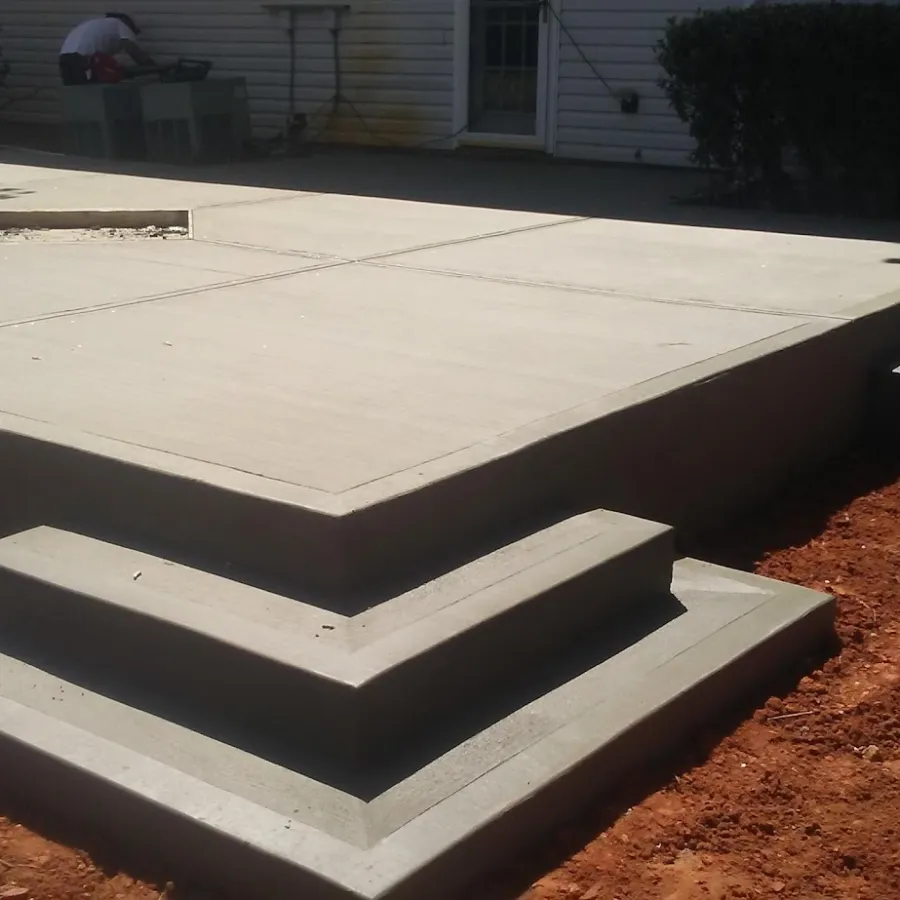 A newly poured concrete patio with steps, featuring clean lines and a smooth surface in a residential setting.