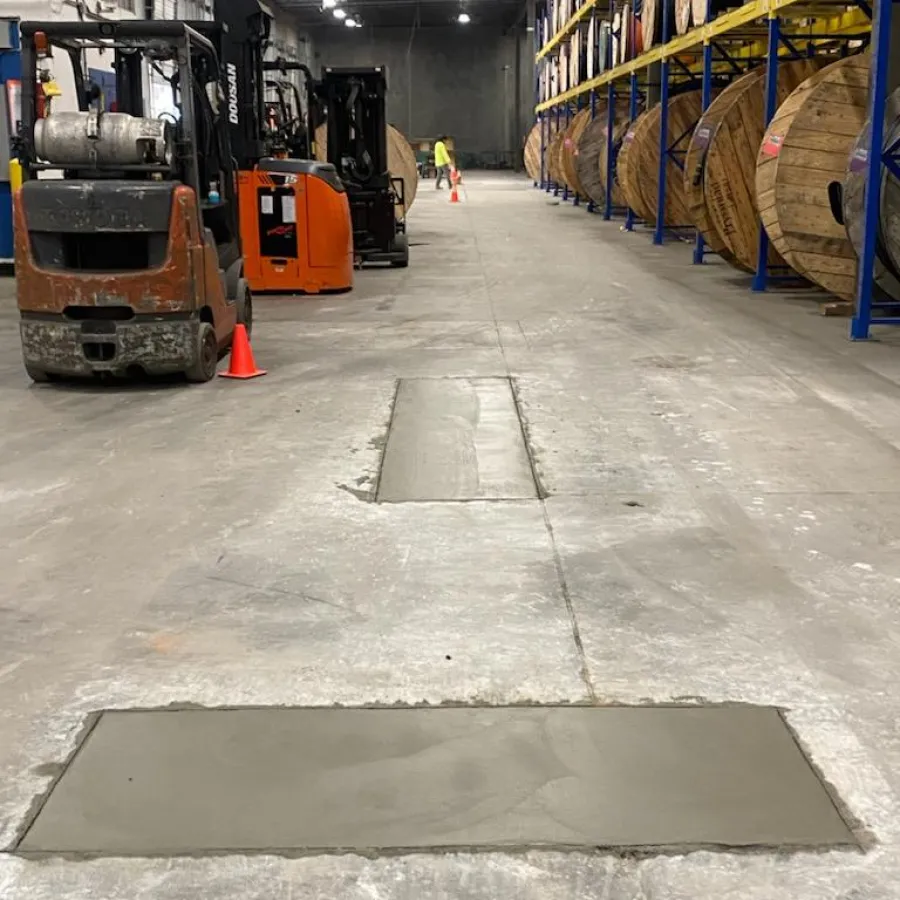 Warehouse interior with freshly poured concrete and wooden barrels on shelves in the background.