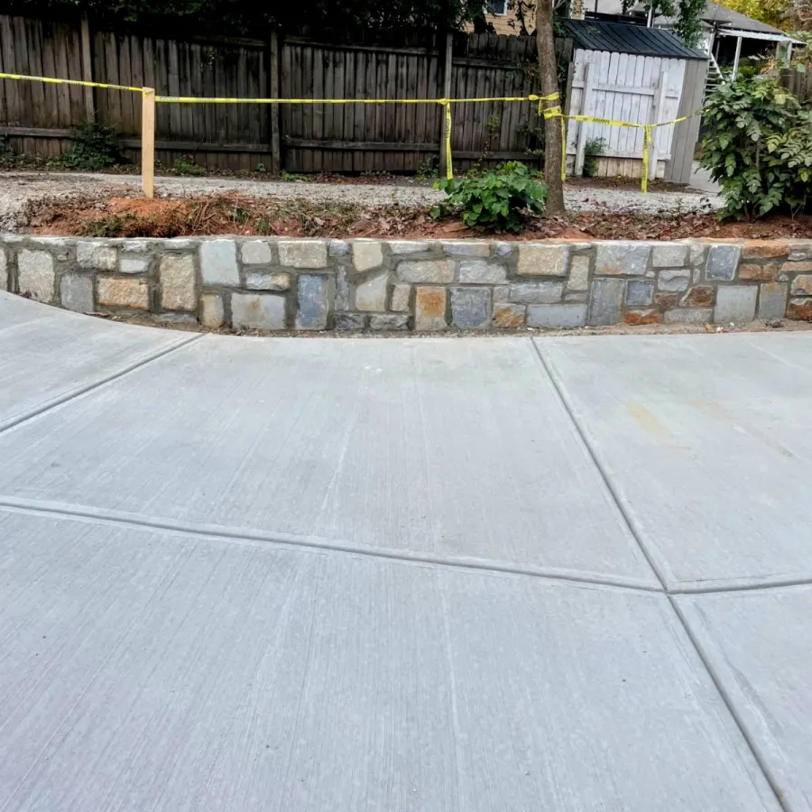 New concrete driveway with decorative stone retaining wall and wooden fence in backyard space.
