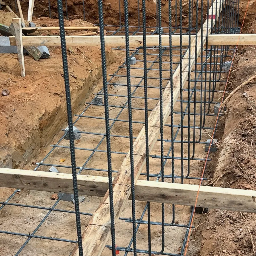Steel rebar framework for foundation reinforcement with wooden braces at a construction site trench.