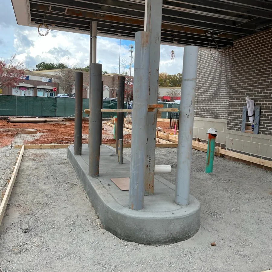 Construction site showing concrete foundation with metal pillars and wooden framing for new building structure.