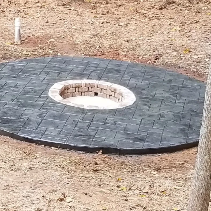 A circular outdoor fire pit area with a stone ring and stamped concrete finish surrounded by gravel.
