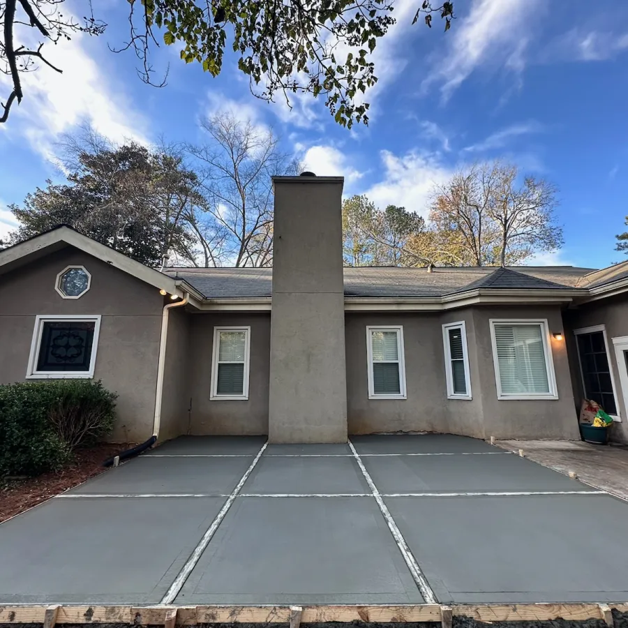 Freshly poured concrete driveway with joint lines in front of a beige suburban house under a blue sky.